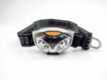 Lampe frontale LED noire et grise, avec un bouton orange et un bandeau réglable noir et gris.