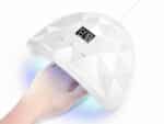 Lampe LED ongle de voyage, spéciale gel UV, allumée avec la main d'une personne. Sur fond blanc.