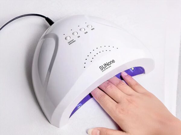 Lampe LED ongle pour vernis simple ou UV, allumée et utilisée par une mannequin, on ne voit que la machine et la main.