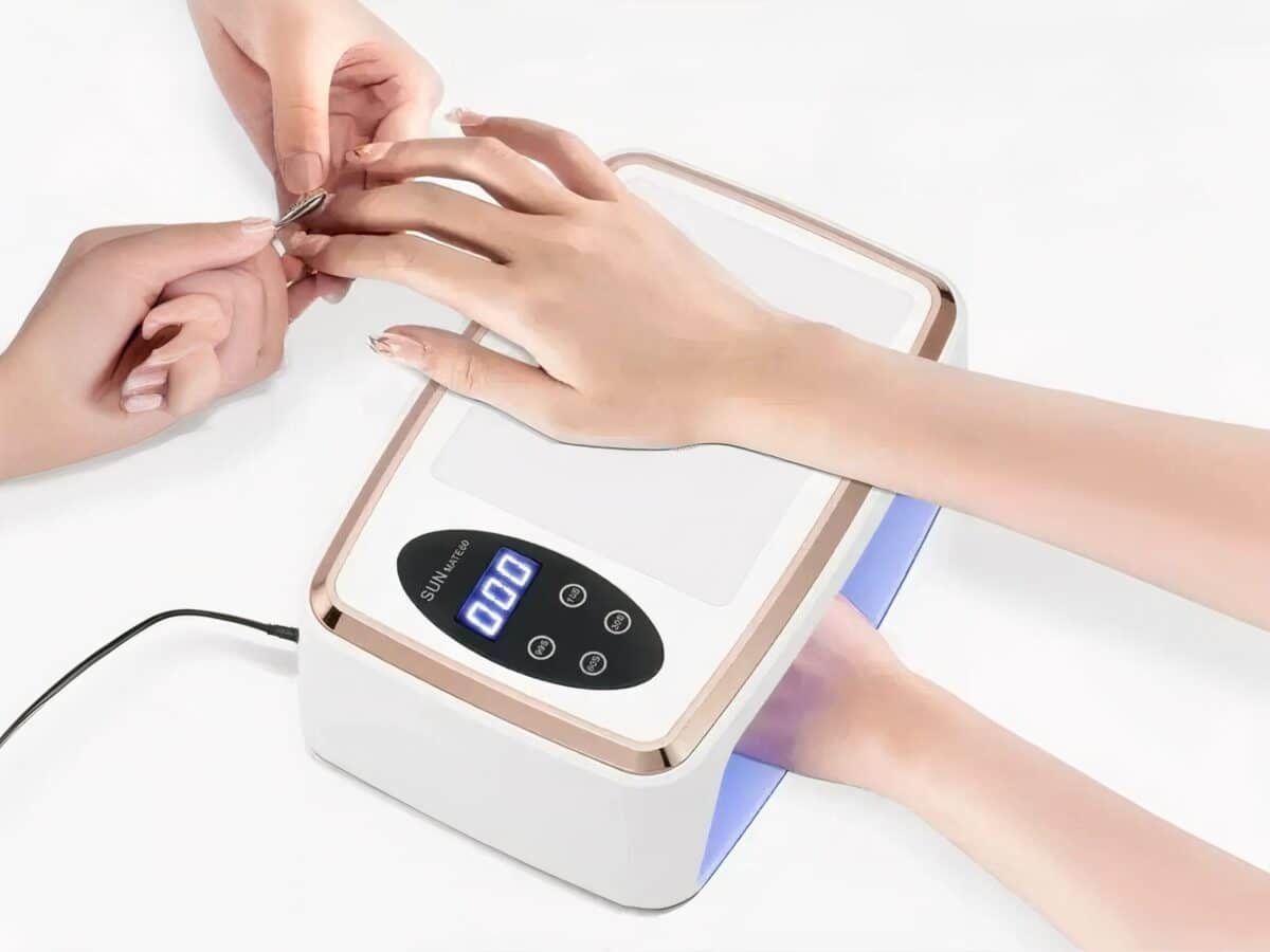 Lampe LED ongle UV grand format Lampe LED ongle UV grand format, blanche et dorée, Utilisée par deux personnes, on ne voit que leurs mains. Une fait la manucure à l'autre.