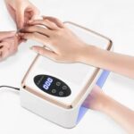 Lampe LED ongle UV grand format, blanche et dorée, Utilisée par deux personnes, on ne voit que leurs mains. Une fait la manucure à l'autre.