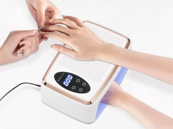 Lampe LED ongle UV grand format, blanche et dorée, Utilisée par deux personnes, on ne voit que leurs mains. Une fait la manucure à l'autre.