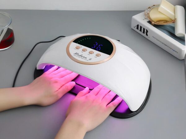 Lampe LED ongle UV allumée, posée sur un bureau gris, avec les 2 mains d'une personne à l'intérieur.