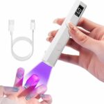 Lampe LED ongle UV mini rechargeable Lampe LED ongle UV portable et rechargeable, allumée et utilisée par une mannequin. On ne voit que ses mains et un câble USB en arrière-plan.