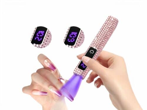 Lampe LED UV mini à strass rose, avec écran tactile, allumée et dans les mains d'une mannequin qui sèche son vernis. On ne voit que ses mains.