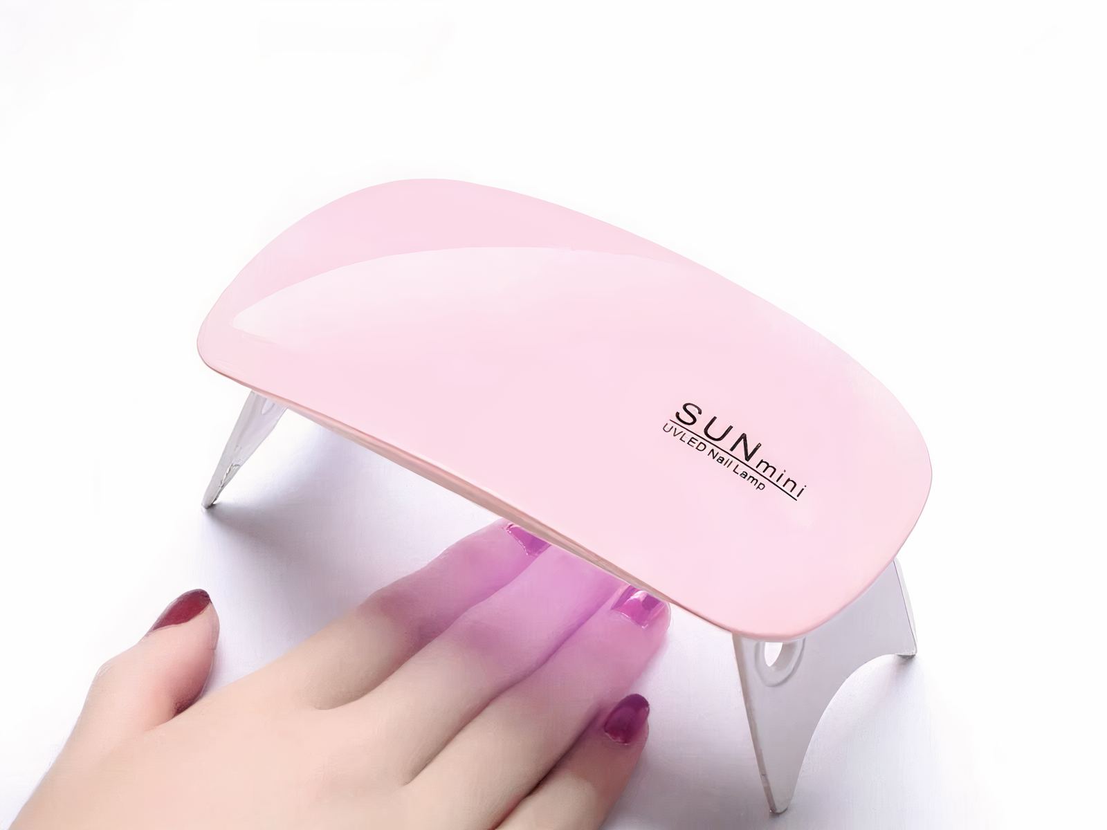 Lampe LED ongles UV pliable et portable, rose et blanche, allumée avec la main d'une femme qui sèche son vernis.