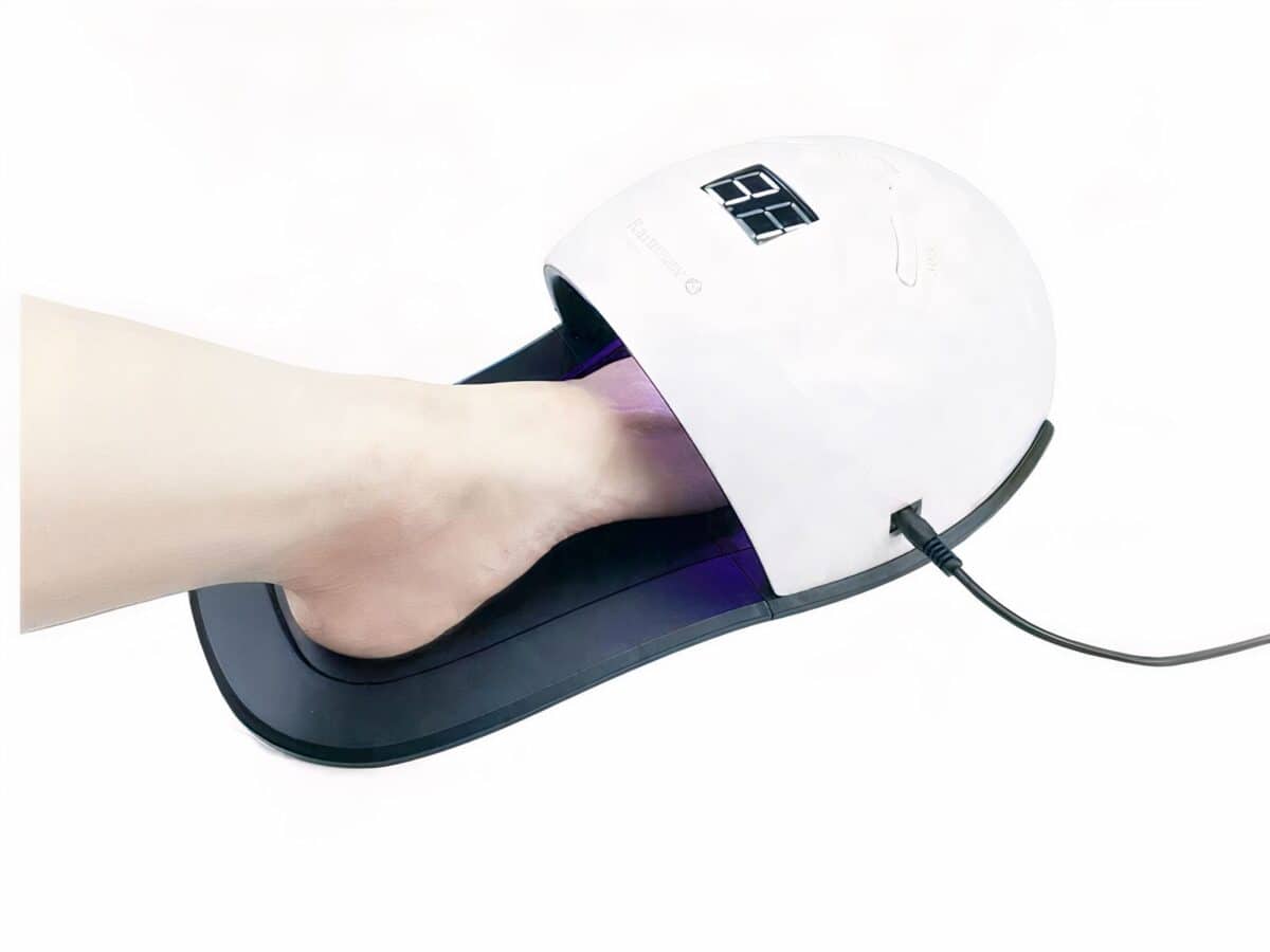 Lampe LED ongle UV ergonomie pied, noire et blanche, avec le pied d'une personne. Sur fond blanc.