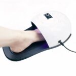 Lampe LED ongle UV pour pieds et mains Lampe LED ongle UV ergonomie pied, noire et blanche, avec le pied d'une personne. Sur fond blanc.