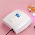 Lampe LED ongle UV rechargeable avec capteur infrarouge Lampe LED ongle UV rechargeable, de dos sur une table rose avec un parfum à côté.
