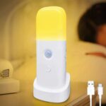Lampe LED rechargeable à détecteur de mouvement posée sur une table de nuit avec une personne allongée dans un lit en fond