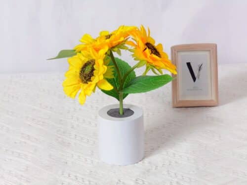 Lampe LED rechargeable effet pot de fleurs posée sur une table avec une nappe blanche et un cadre en fond