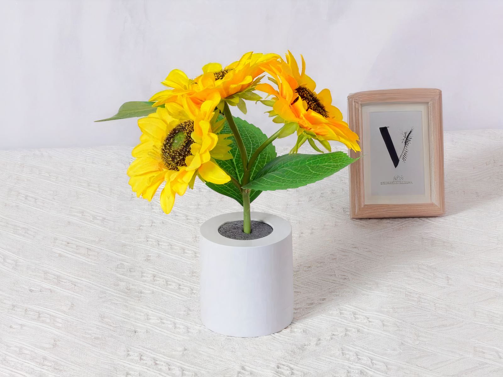 Lampe LED rechargeable effet pot de fleurs posée sur une table avec une nappe blanche et un cadre en fond