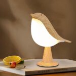 Lampe LED rechargeable style oiseau en bois posée sur un livre avec une rondelle de citron