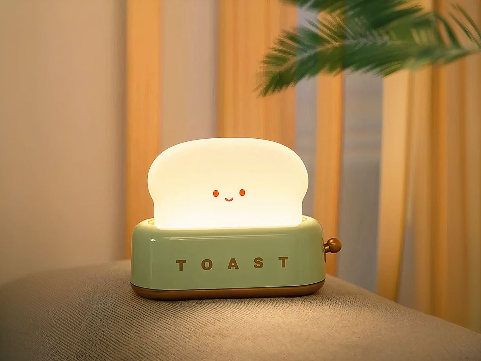 Lampe LED sans fil amusante style grille-pain posée sur un support gris avec des feuilles de palmier en fond