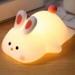 Lampe LED sans fil et rechargeable style lapin Lampe LED sans fil et rechargeable style lapin sur une table en bois marron avec un livre en fond