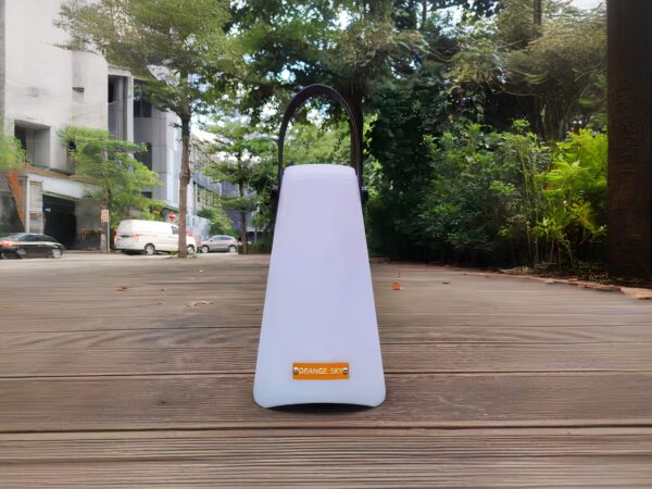 Lampe LED sans fil télécommandée et étanche posée en extérieur avec des arbres et des buissons en fond