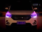 Voiture blanche, dans un espace sombre, avec les deux rubans LED installés sur les phares et allumés en violet.
