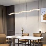 Lustre LED vague dorée suspendue Lustre LED vague doré suspendue au-dessus d'une table blanche, avec des chaises autour.