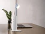 Mini lampe LED design avec son support de transport, sur un bureau à côté d'un ordinateur.