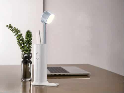 Mini lampe LED design avec son support de transport, sur un bureau à côté d'un ordinateur.