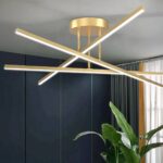 Plafonnier LED minimaliste moderne Plafonnier LED minimaliste moderne doré, trois bâtons qui s'entrent-croise. Installé sur un plafond gris clair.
