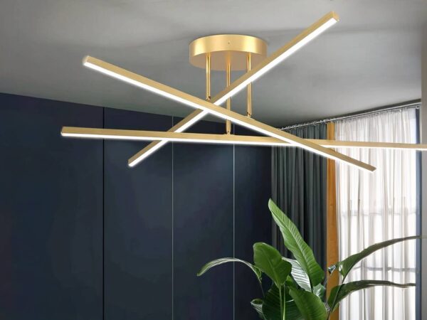 Plafonnier LED minimaliste moderne doré, trois bâtons qui s'entrent-croise. Installé sur un plafond gris clair.