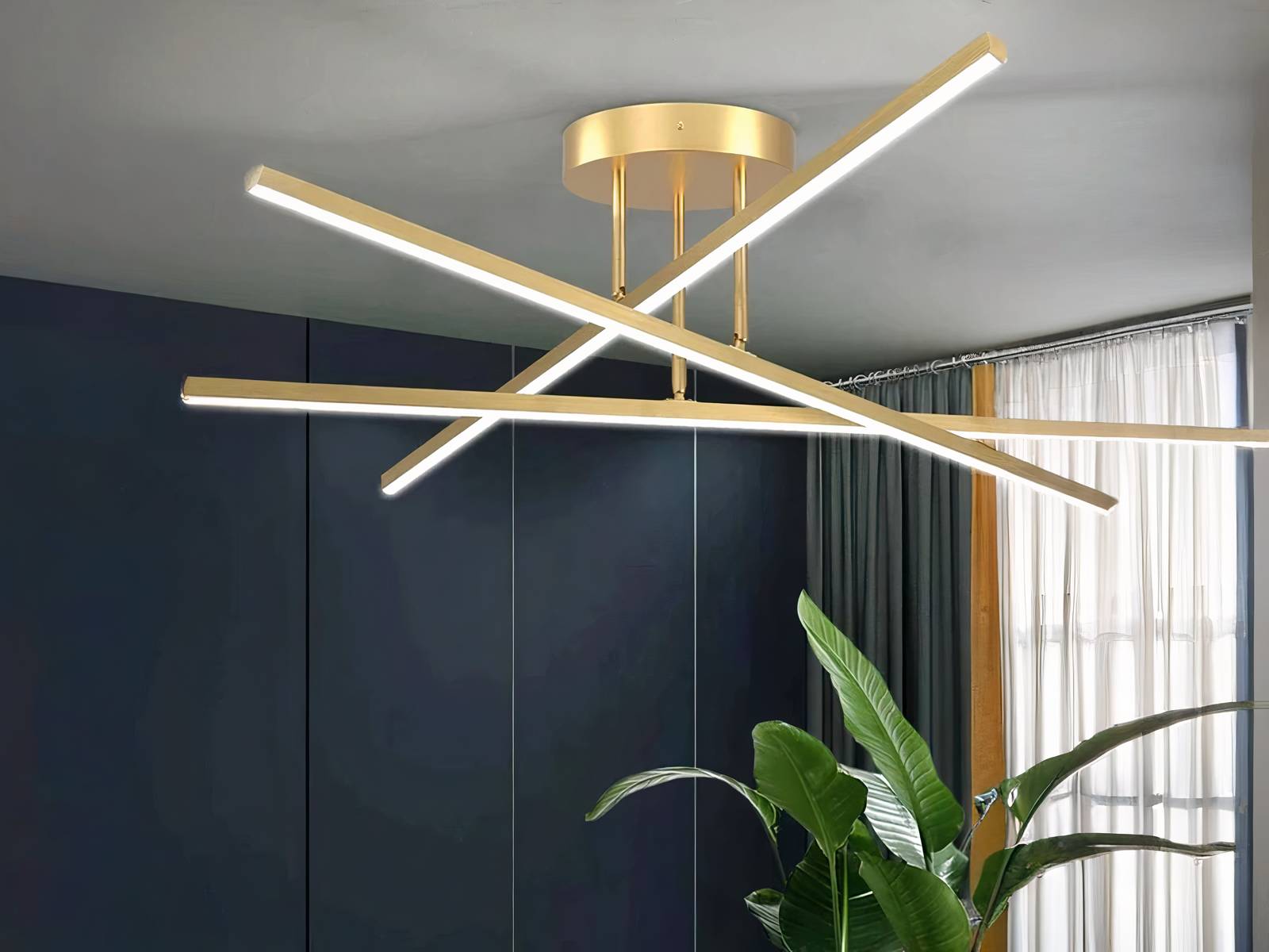 Plafonnier LED minimaliste moderne doré, trois bâtons qui s'entrent-croise. Installé sur un plafond gris clair.