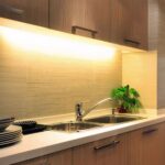 Réglette led cuisine sur batterie avec capteur de mouvement Réglette LED cuisine allumée et installée sous un meuble haut de cuisine au-dessus d'un évier.