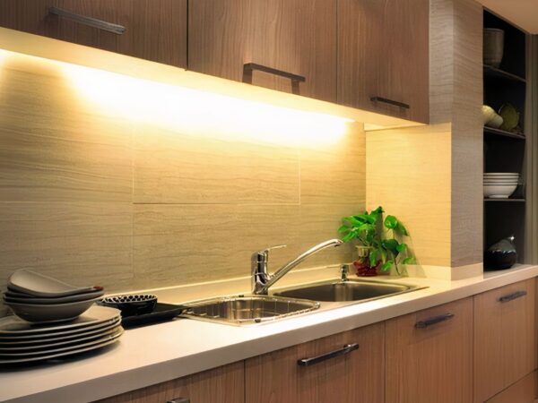Réglette LED cuisine allumée et installée sous un meuble haut de cuisine au-dessus d'un évier.