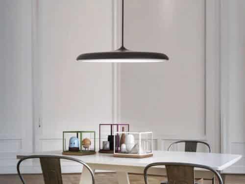 Suspension LED design en forme de soucoupe noire, au dessus d'une table de salle à manger.