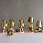 Veilleuses LED tactiles dorées, en forme de personnage dans des postures assises ou debouts avec un abat-jour brillant, apportant une lumière douce et une touche moderne à votre espace