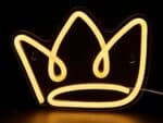 Couronne néon LED en silicone fixée au mur, émettant une lumière chaude, alimentée par un câble USB. La forme de couronne brille doucement.