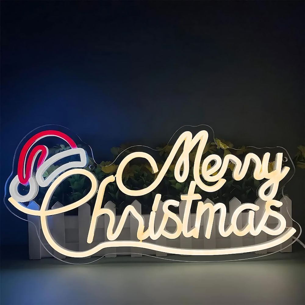 Une enseigne lumineuse néon LED représentant Merry Christmas sur deux lignes. La lettre C de christmas est surmonté d'un chapeau de père noël lumineux blanc et rouge.