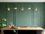 Le lustre à led doré au design moderne au-dessus d'une table de salle à manger en bois au fond un mur vert