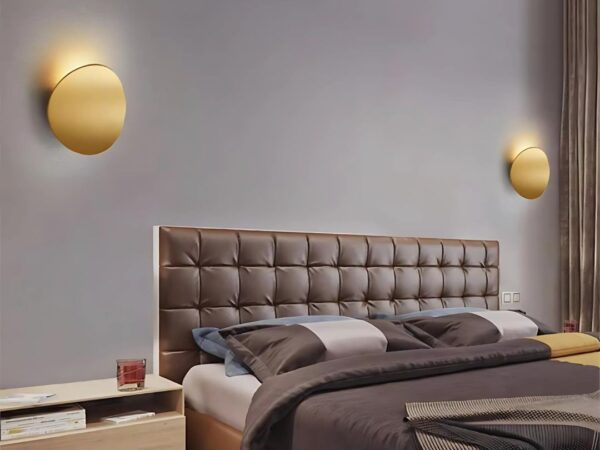 Les deux appliques murales en aluminium en doré de chaque côté d'un lit sur un mur taupe.