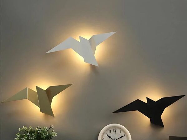 Les trois modèles d'appliques murales LED en forme d'oiseau doré, blanc et noir au-dessus d'un bureau avec une horloge, sur un mur taupe.