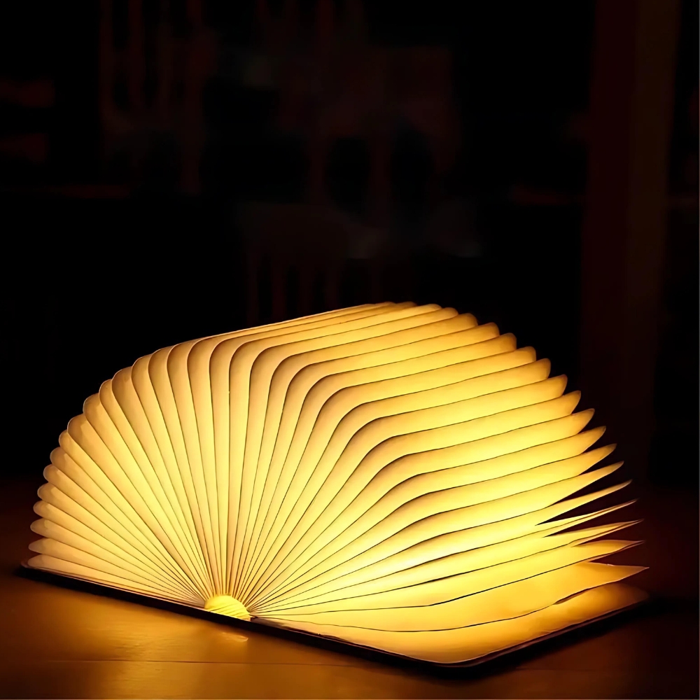 Lampe de chevet LED en forme de livre ouvert. La lumière est diffusée à travers les pages en papier. Sur fond noir.