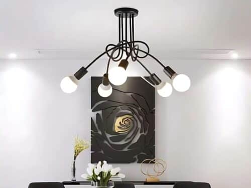 Lustre LED au style vintage au-dessus d'une table de salle à manger noire. Sur le mur blanc du fond il y a un grand cadre noir et doré.