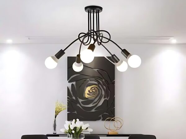 Lustre LED au style vintage au-dessus d'une table de salle à manger noire. Sur le mur blanc du fond il y a un grand cadre noir et doré.