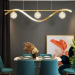 Lustre LED doré avec trois globes en verre Le lustre doré avec trois globes en verre au-dessus d'une table de salle à manger avec des chaises bleu canard.