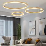 Lustre LED suspendu moderne à trois anneaux Le lustre LED suspendu moderne à trois anneaux dans un salon avec deux tableaux sur le mur , une grande baie vitrée avec un rideau gris.