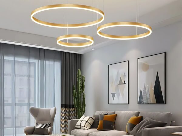 Le lustre LED suspendu moderne à trois anneaux dans un salon avec deux tableaux sur le mur , une grande baie vitrée avec un rideau gris.