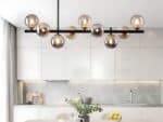 Le lustre suspension en verre au style contemporain dans une cuisine au dessus d'une grande table blanche dessus avec une plante verte et un saladier avec des citrons jaunes