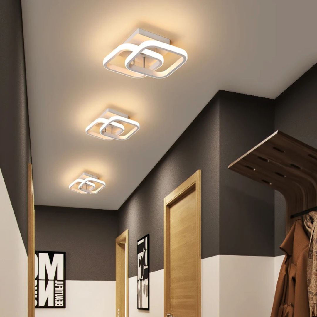 3 plafonniers LED double carré dans un couloir avec deux portes en bois clair.