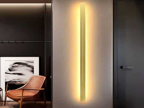 L'applique murale LED pour salon est installée sur un mur blanc où se trouve un fauteuil couleur rouille devant une toile noire et blanche.