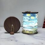 Lampe de chevet LED pliable de style lanterne japonaise Lampe de chevet LED pliable style lanterne japonaise aux motifs bleus et verts. Pliable en forme accordéon. Les deux extrémités sont en bois foncé. Une lampe pliée se trouve à gauche de la lampe ouverte et allumée. Elles sont posées sur une surface type marbre blanc. Un mur gris en fond.