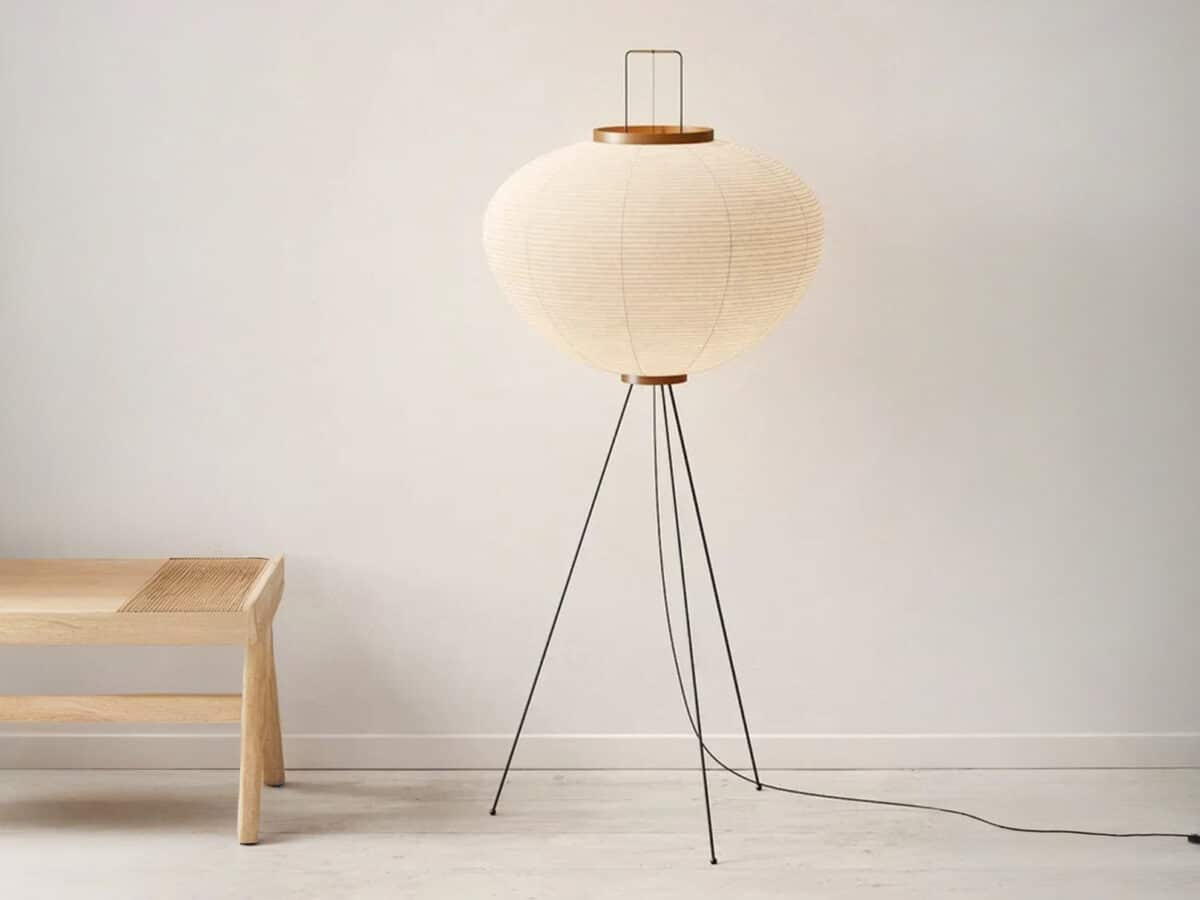 Lampadaire LED japandi minimaliste chic en papier de riz blanc délicatement façonné et son trépied noir métallique sur fond uni beige