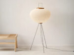 Lampadaire LED japandi minimaliste chic en papier de riz blanc délicatement façonné et son trépied noir métallique sur fond uni beige