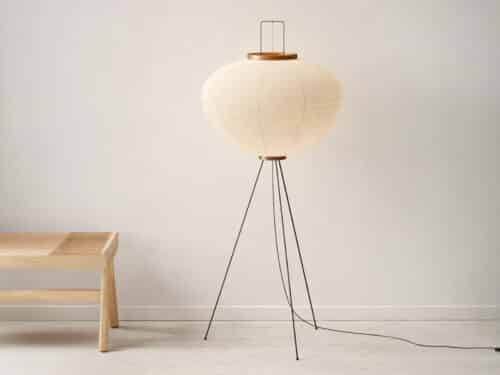 Lampadaire LED japandi minimaliste chic en papier de riz blanc délicatement façonné et son trépied noir métallique sur fond uni beige