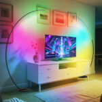 Lampadaire LED d’angle arqué intelligent Deux lampadaires LED d’angle arqué intelligent noir mat avec lumière RGB personnalisable au design moderne et élégant, installés dans un salon de par et d'autre la télévision.